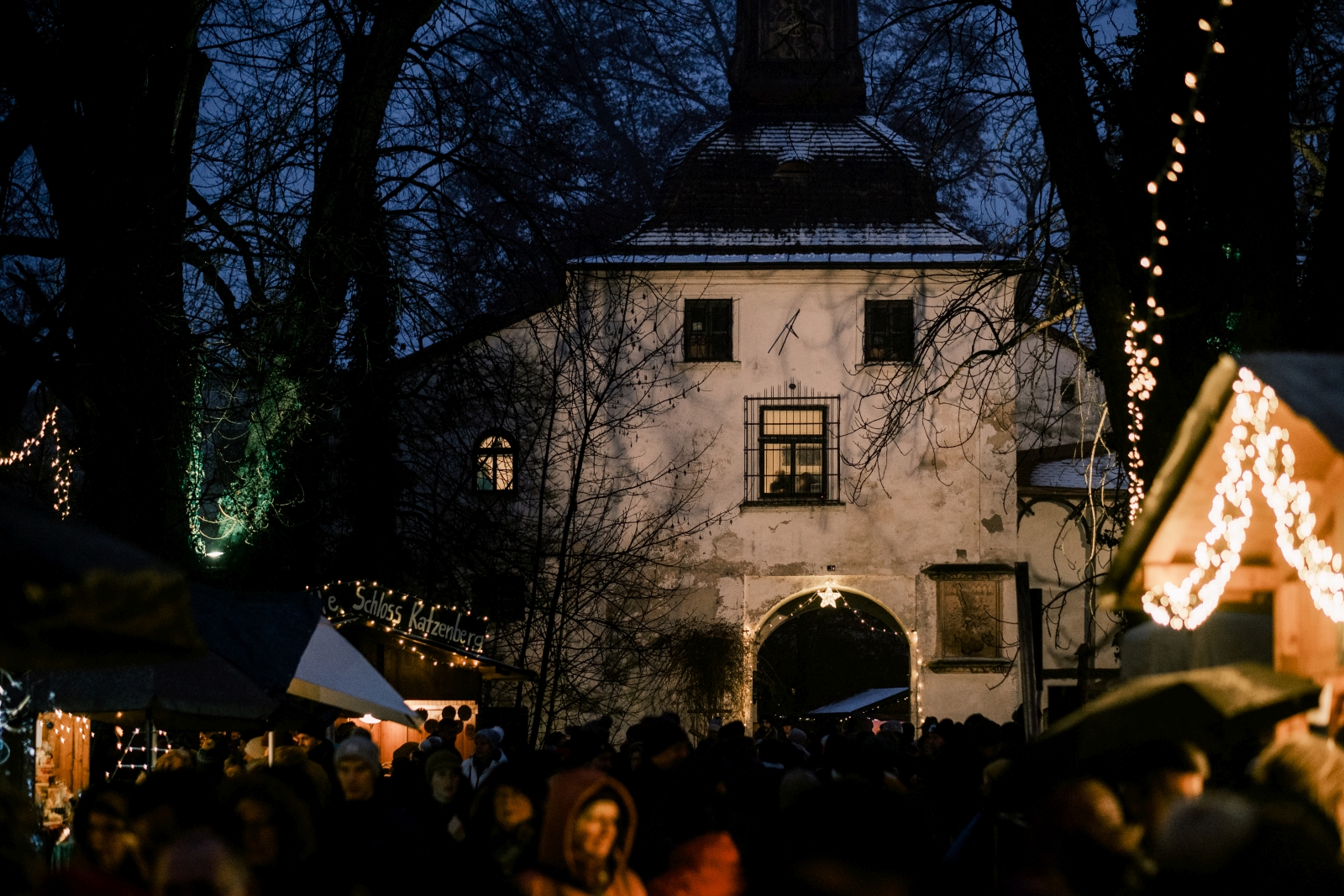 Schlossportal in der Nacht, festlich beleuchtet, davor Weihnachtsmarkthütten