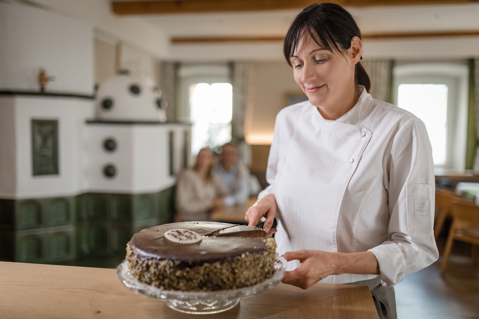 Frau in Kochjacke schneidet Schokotorte mit Kürbiskernrand an