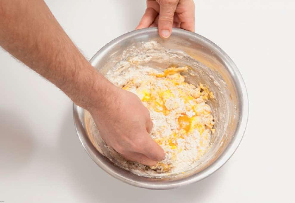 Mehl und weitere Zutaten in großer Schüssel werden mit Händen verarbeitet