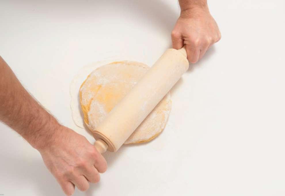 Bemehlter Teig wird mit Nudelwalker ausgerollt