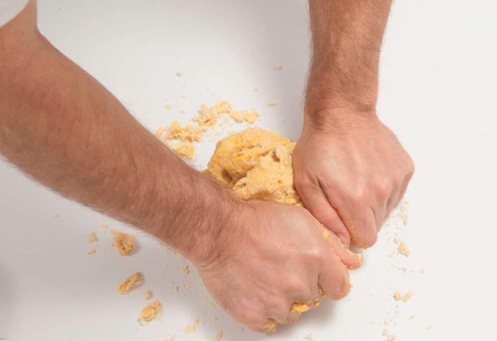 Nudelteig wird mit Händen auf Arbeitsfläche geknetet