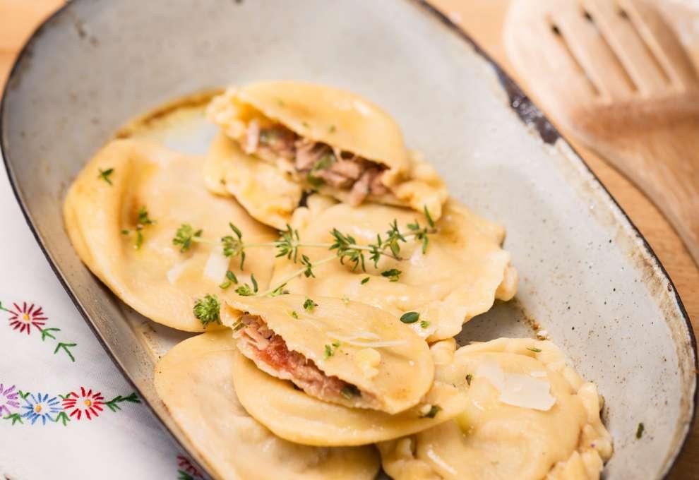 mehrere Nudeltascherl, eines davon aufgeschnitten, mit Thunfischfülle auf länglichem Teller