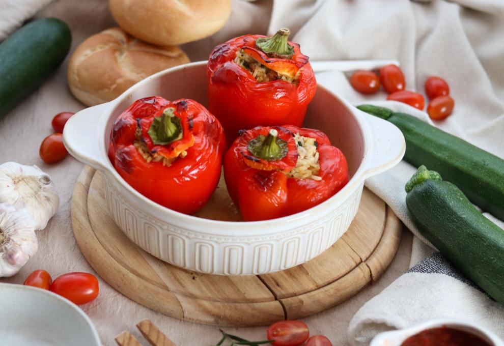 Drei gefüllte, rote Paprika in weißer Auflaufform