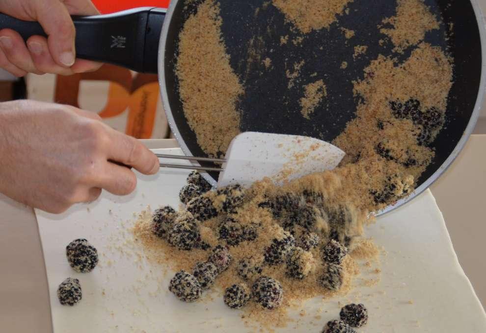 Brösel-Brombeerfülle kommt aus Pfanne auf ausgerollten Blätterteig