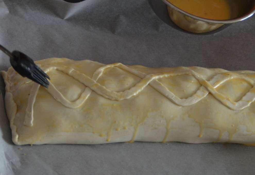 Fertiger Blätterteigstrudel wird mit verquirltem Ei bestrichen.