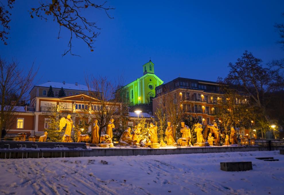 Große Weihnachtskrippe im Freien, dahinter weihnachtlich beleuchtete Häuse und Kirche
