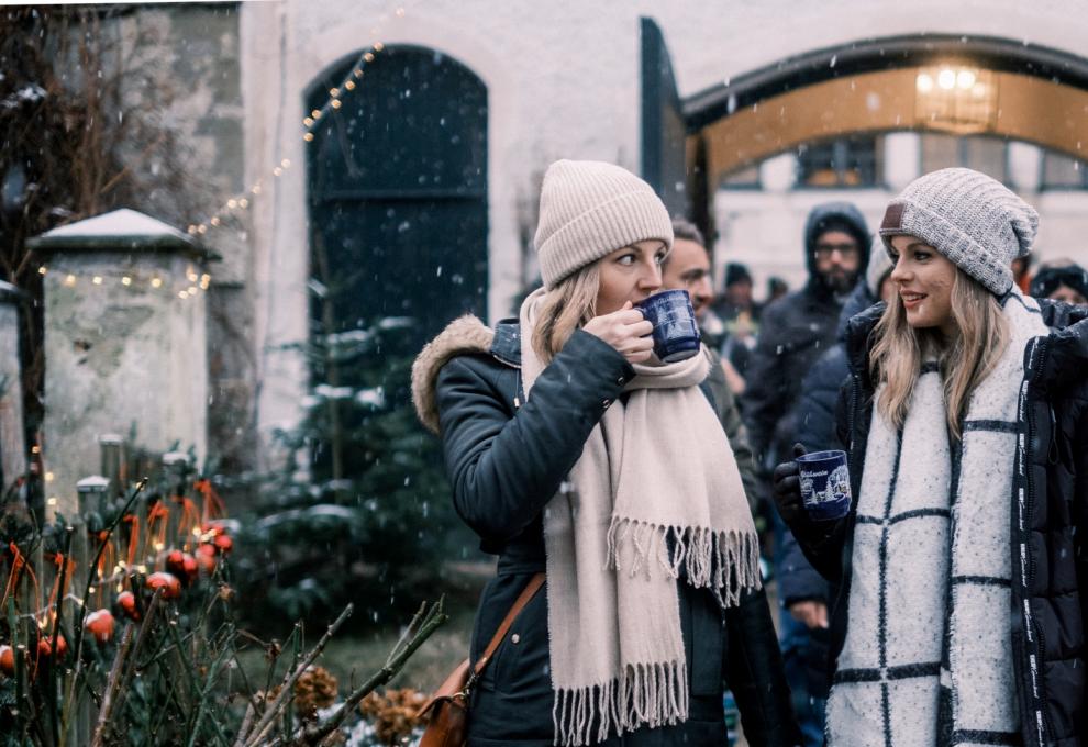 Zwei junge Frauen im Freien, weihnachtlich dekoriert, mit Glühweintassen in der Hand
