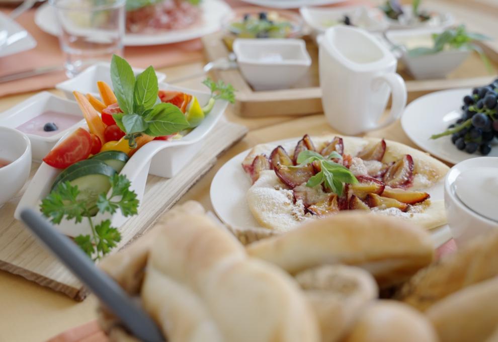 Zwetschkendatschi und frisches Gemüse am Frühstückstisch, dazu Joghurt und Brot, im Hintergrund Milch und Obst